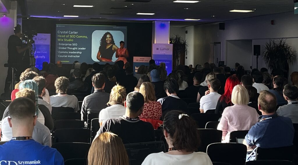 Crystal Carter, Head of SEO Comms at Wix, presenting on the Lumar Stage at BrightonSEO 2024. Photo shows a full, packed room full of attendees for this talk on increasing brand visibility in LLMs and generative search tools.